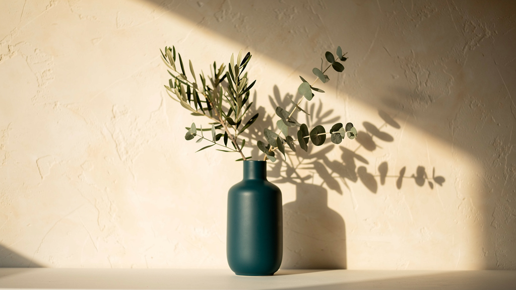 Green branches in a teal vase in warm daylight.