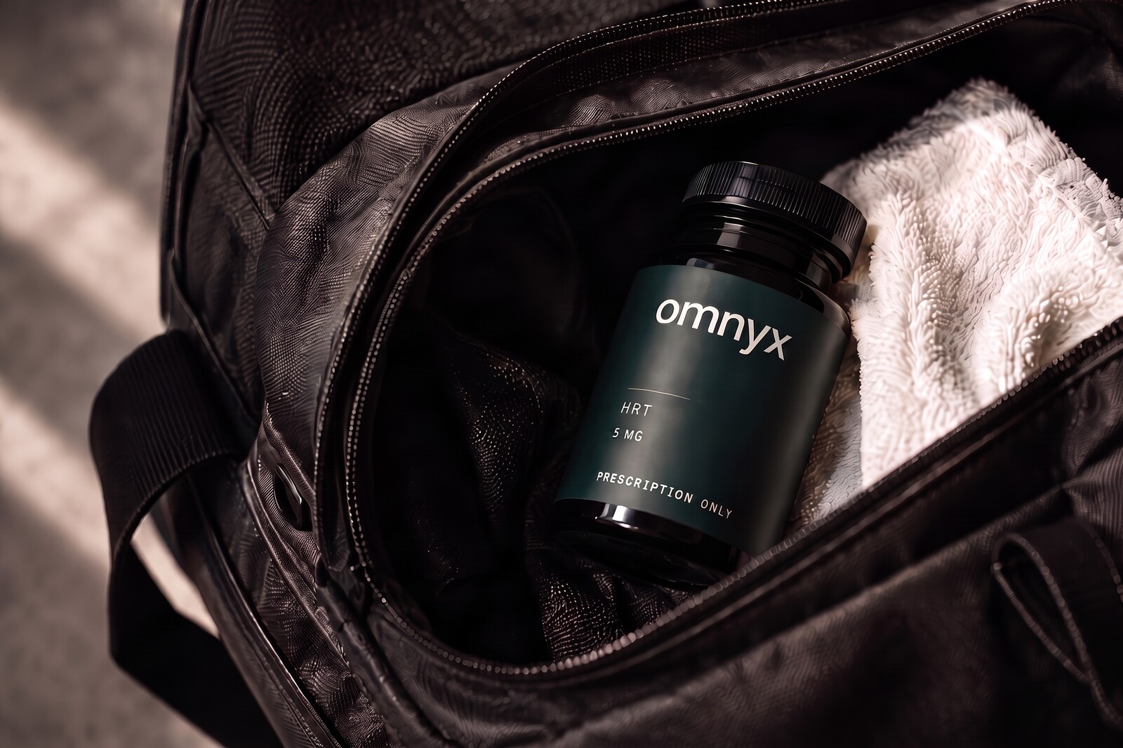 An omnyx prescription bottle tucked into a black gym bag beside a white towel, in warm directional light.